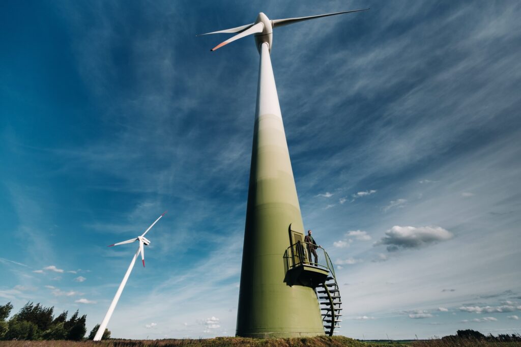 A man in a business suit with a green Golf shirt stands next to a windmill against the background of